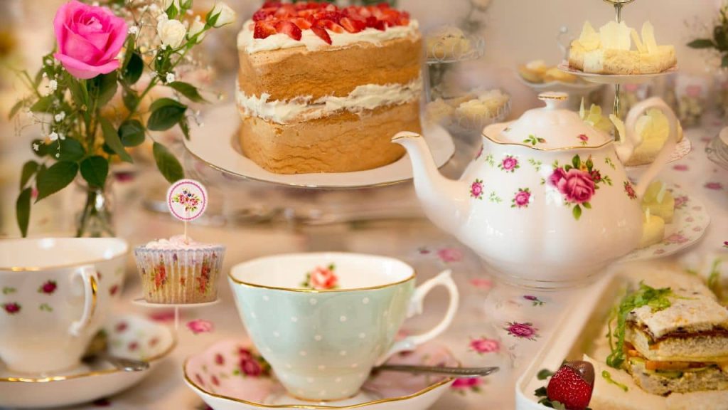 A high tea setup, including a teapot and two cups, finger sandwiches, and a Victoria sponge.