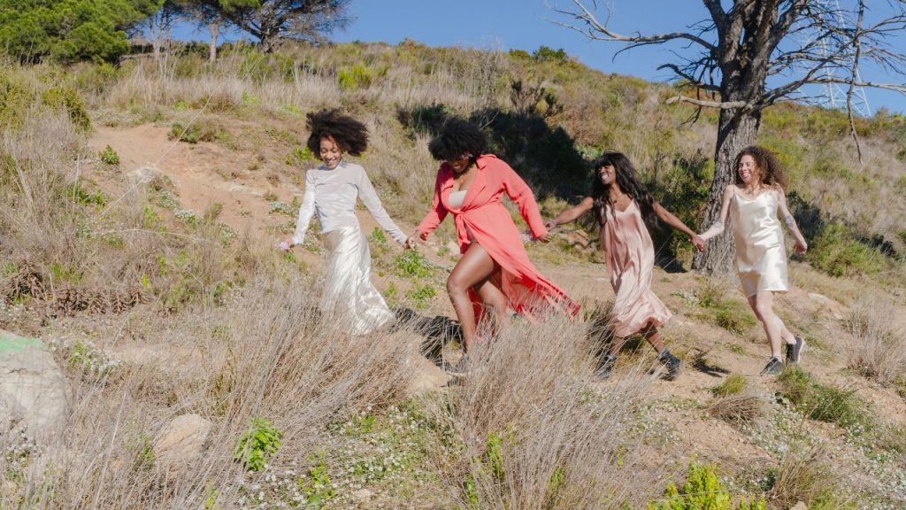 Four women hold hands as they run through a field.