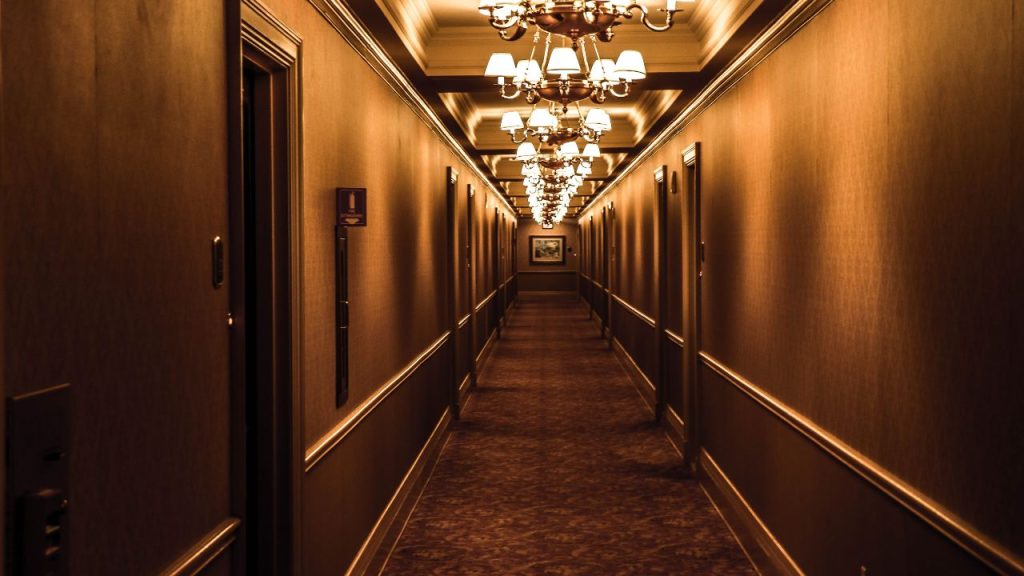 A hotel hallway is lit by chandeliers.