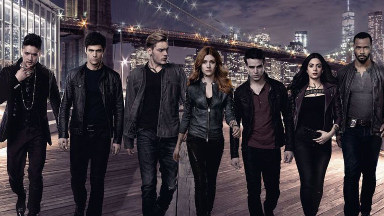 Shadowhunters TV show poster with Magnus, Alec, Jace, Clary, Simon, Isabelle, and Luke all walking forward in black clothes and leather.