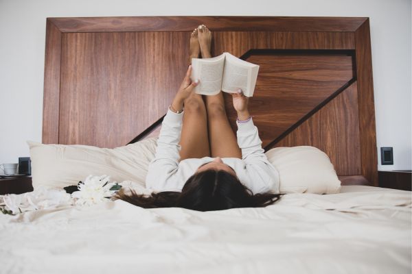 woman reading on a bed with her legs up on the headboard.