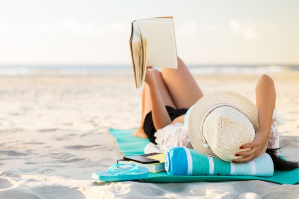 woman reading while laying on the beach.