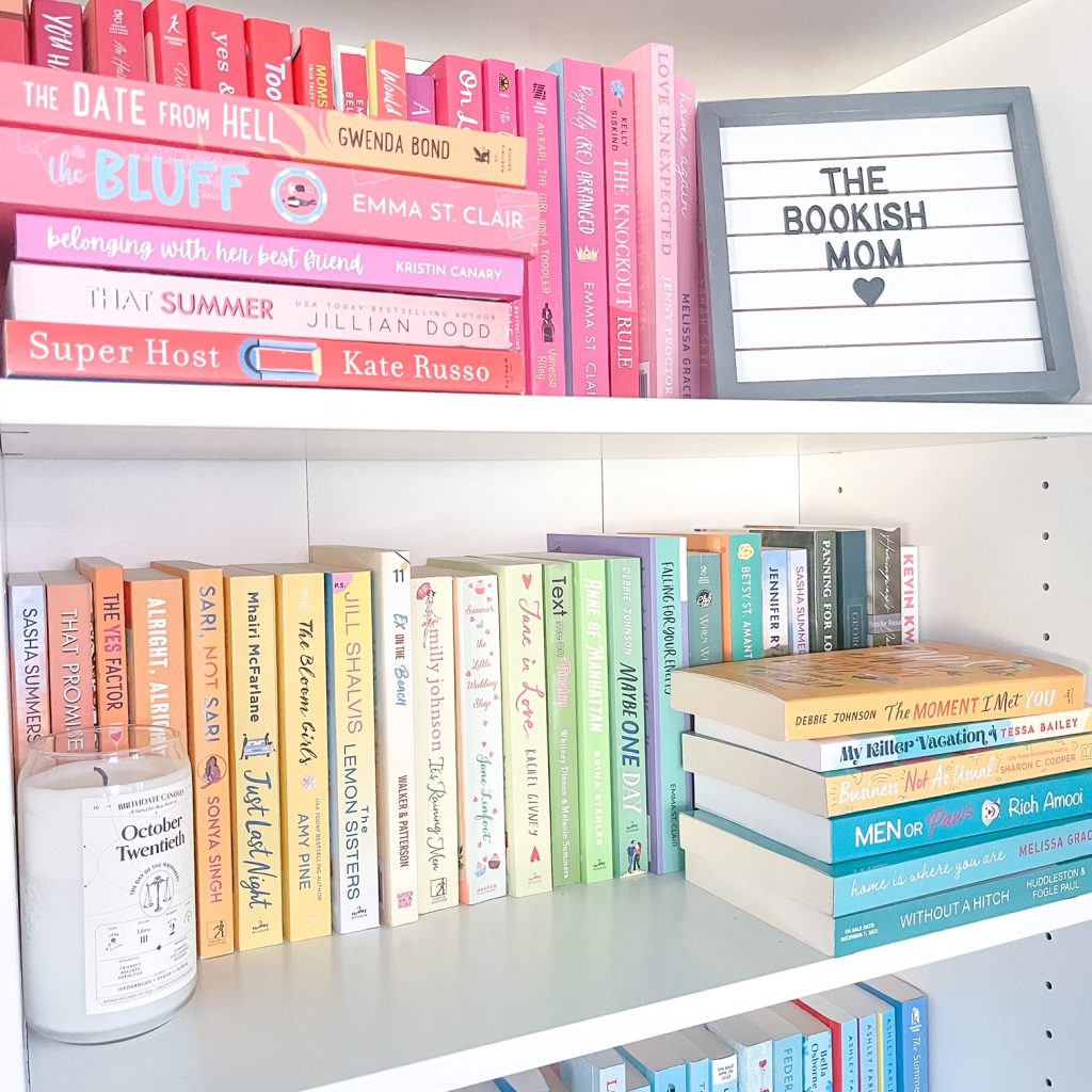 Bookstagrammer Molly of @the.bookish.mom's miminalist bookshelf with books arranged in a gradient of pink, yellow, and blue, and a frame featuring her Bookstagrammer handle.