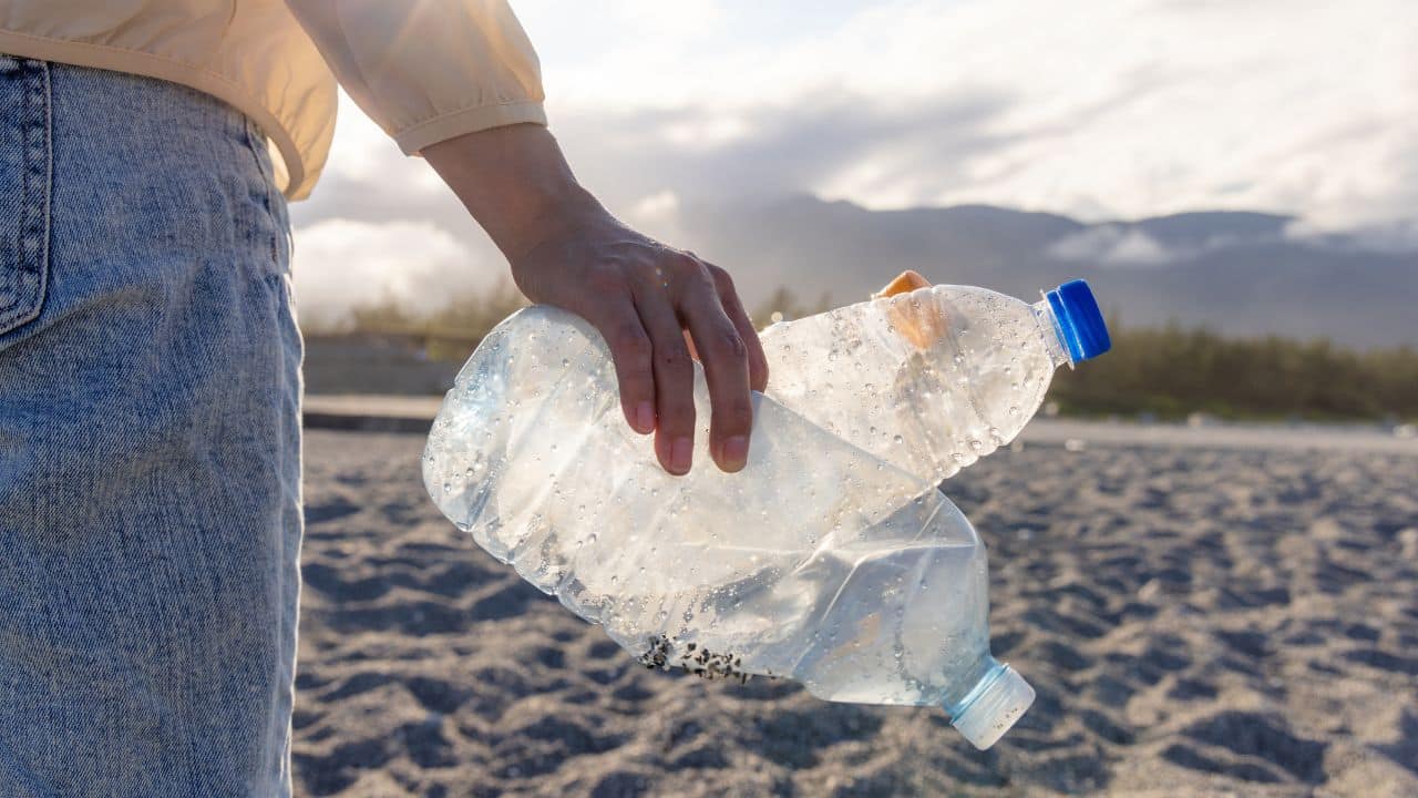 Two plastic bottles held in a persons hand on a beach.