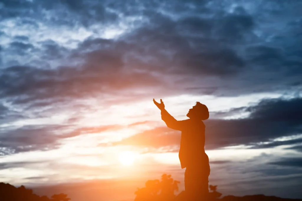 Man praying to the sky during sunset.