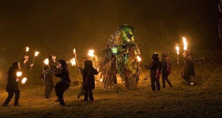 People out at night with torches surrounding a wicker man statue