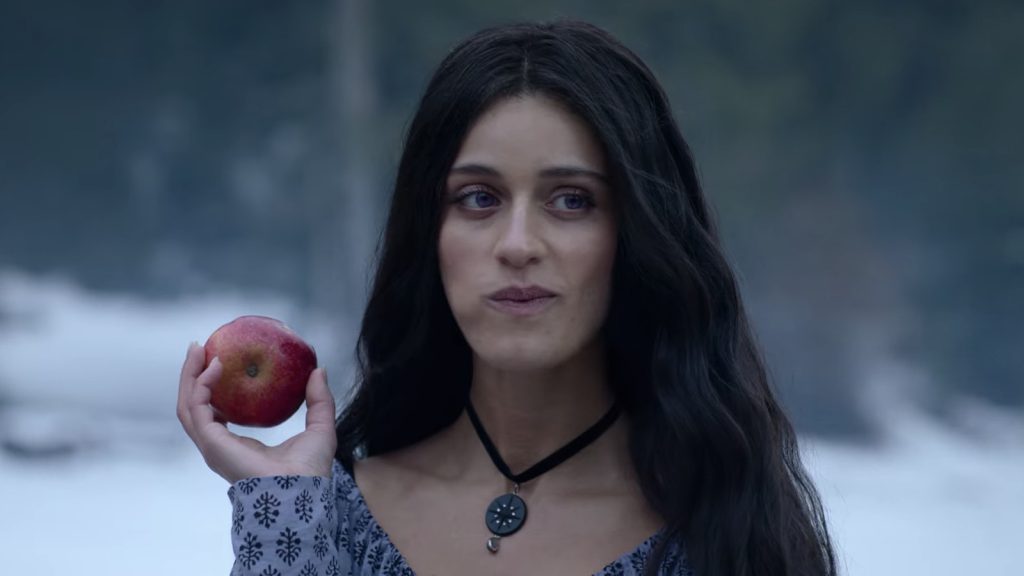 Yennefer of Vengerberg from the TV series "The Witcher" is eating an apple while wearing a purple dress. 