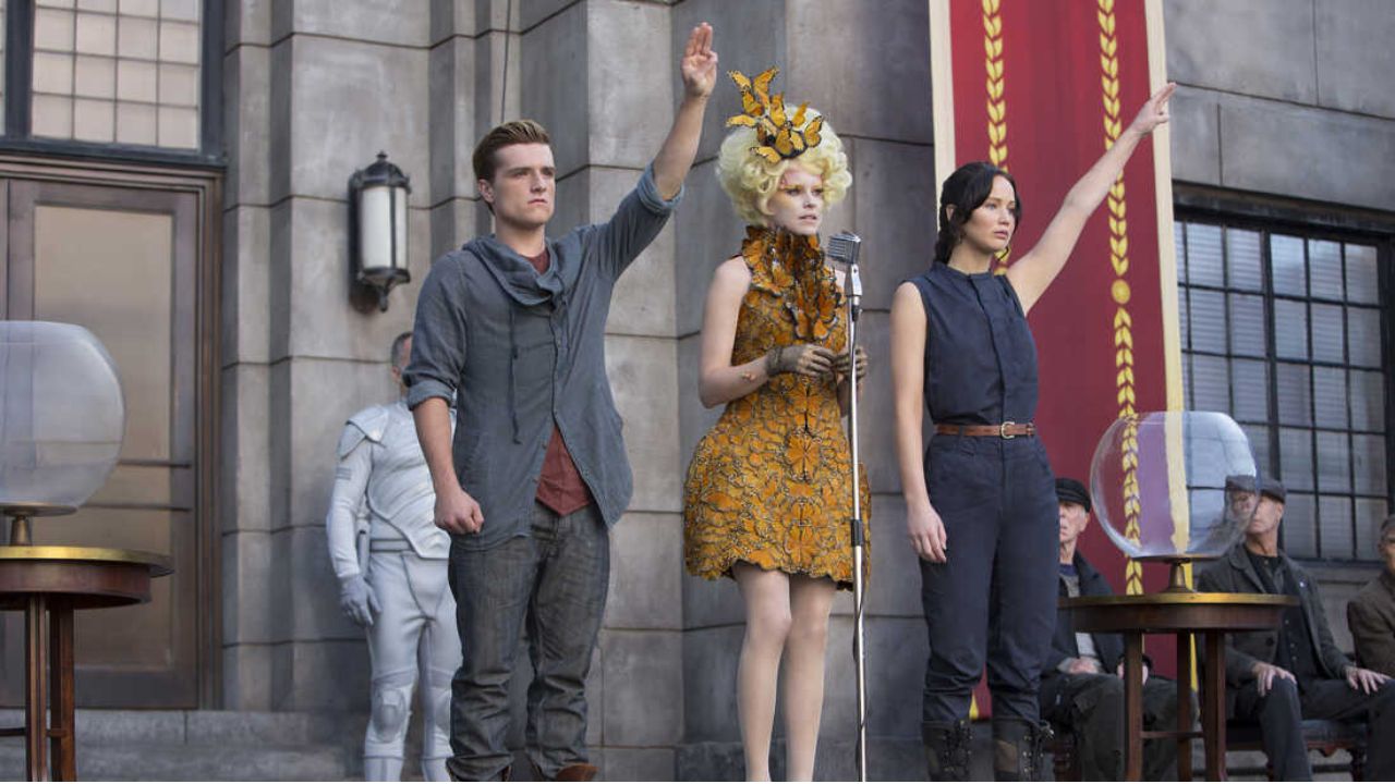 catching fire Peeta, Effie, and Katniss at the Reaping putting their two fingers up in the air.