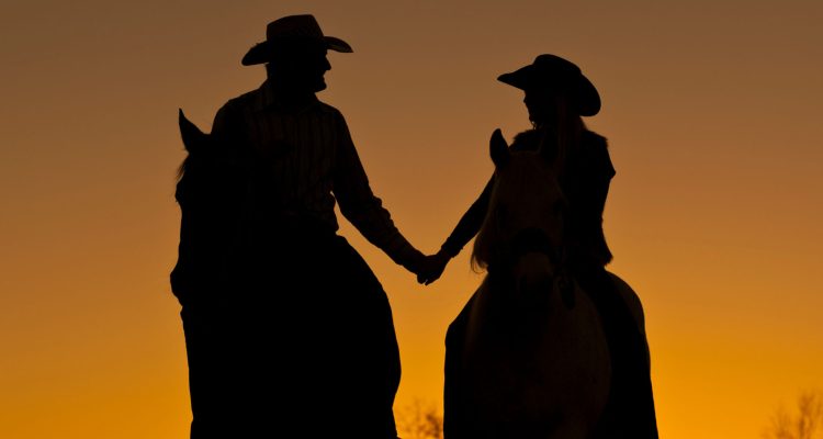 sunset silhouette of a cowboy couple on horseback
