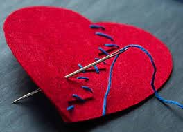 A red heart stitched together with blue thread and a needle sticking through it