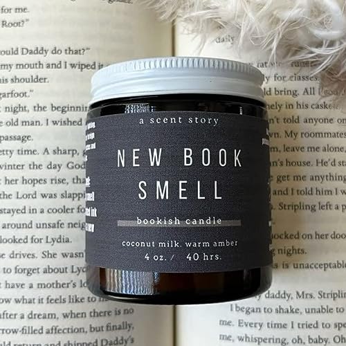 A book is open with a fluffy pillow on the top right. In the middle is a black candle with a gray packaging strip that says new book smell