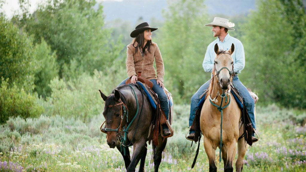 Modern cowboy and cowgirl riding on a pasture on horses.