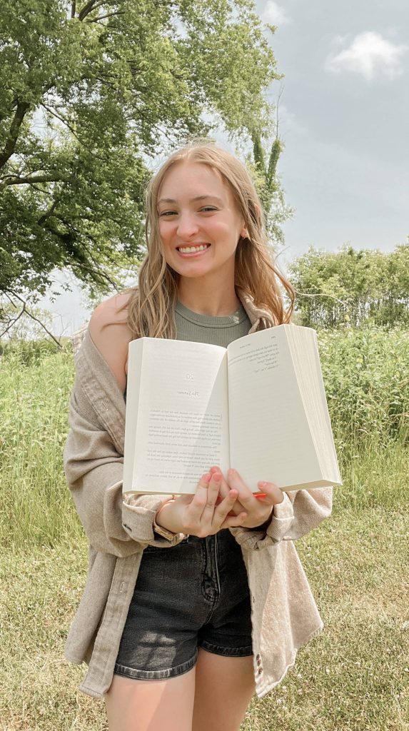 @librarybyemily standing in a field holding an open book