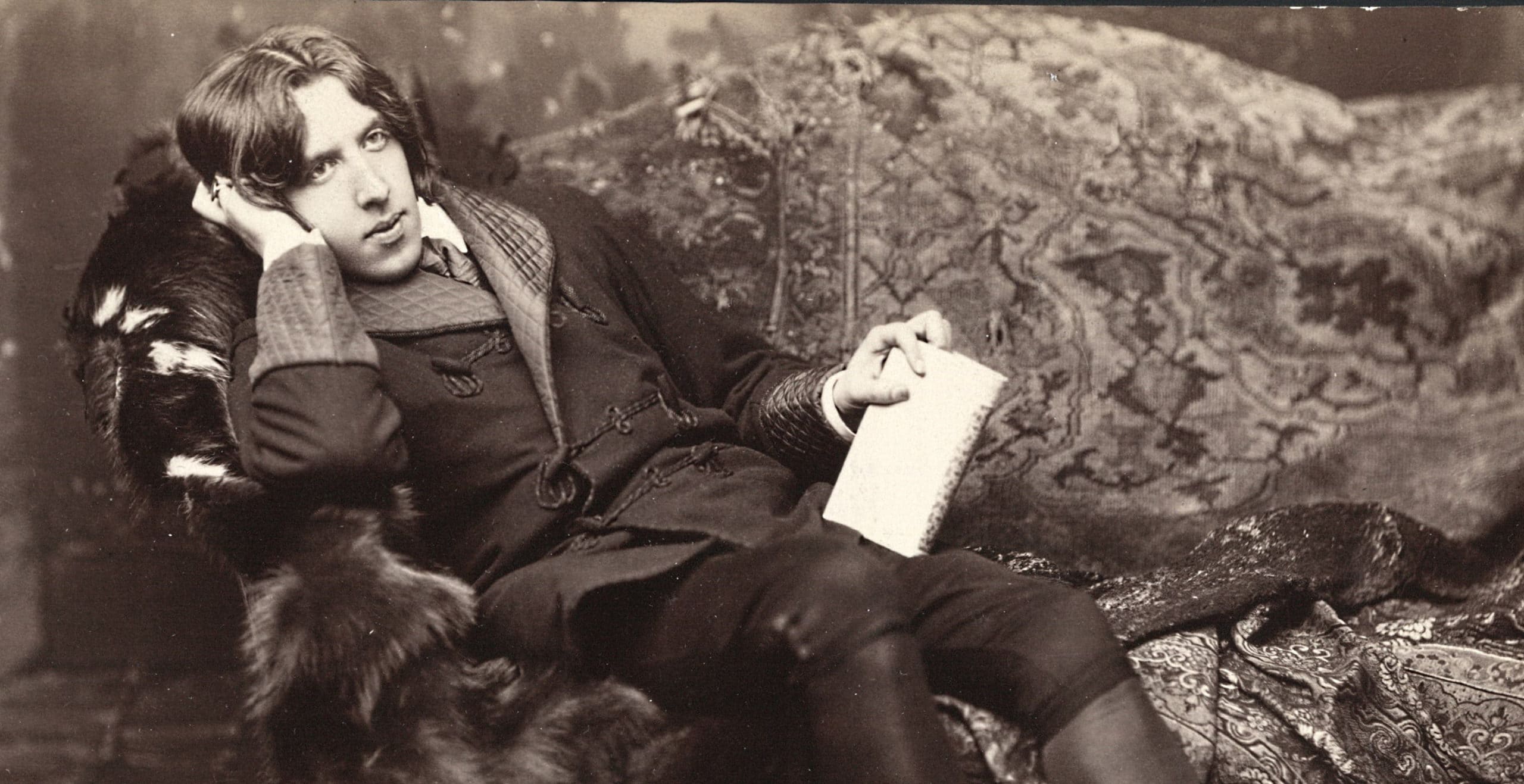 Oscar Wilde reclining on sofa and holding book