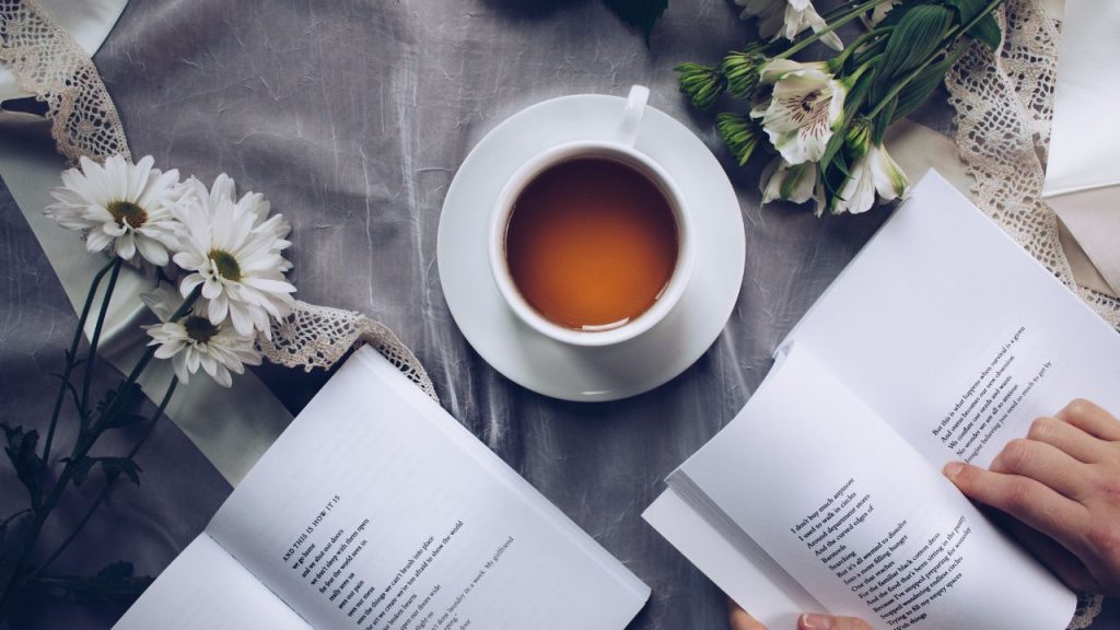 Table set with tea and flowers as hands hold open a book of poetry.