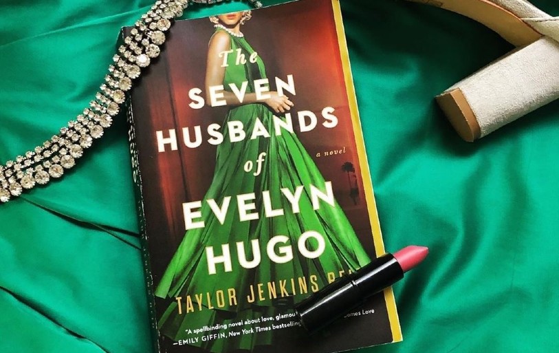 Serious Women Cover book the Seven Husbands of Evelyn Hugo that features Evelyn in a green dress a Pearl neckless and shows her red clips and blonde hair 
