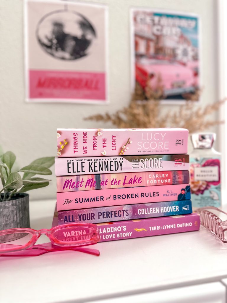 Bookstagrammer Sara's books stacked up in a gradient of pink beside a plant, pink sunnies, and a pink clutcher