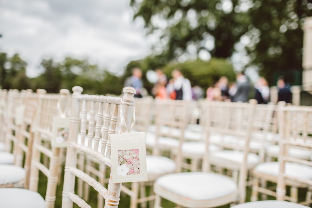 White chairs at a wedding with a wedding decal hooked on the chair.