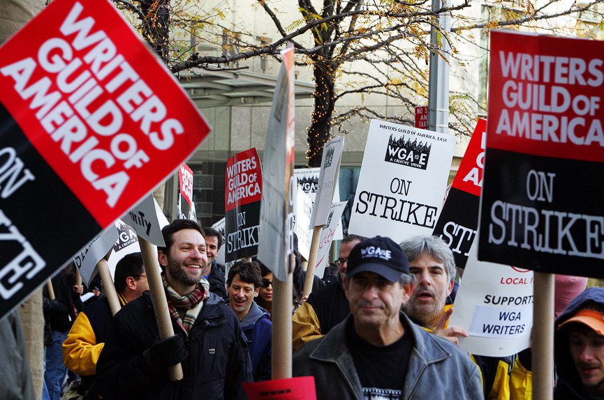 Writers walking down the street holding signs saying "Writers Guild of America on strike"
