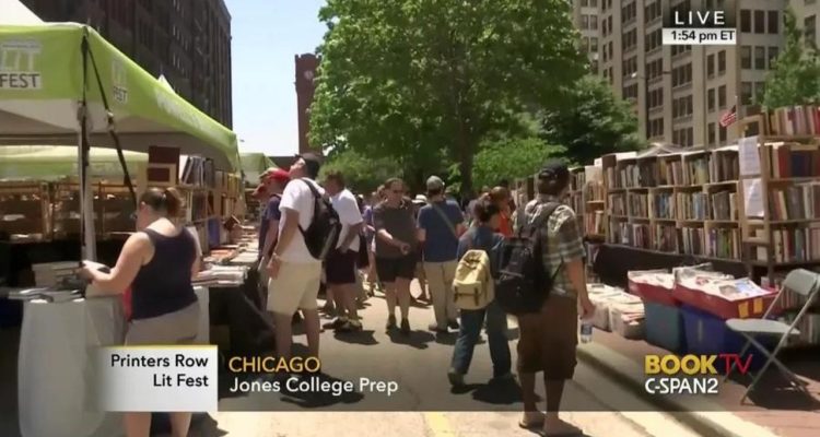 people walk down street filled with book shelves and tents