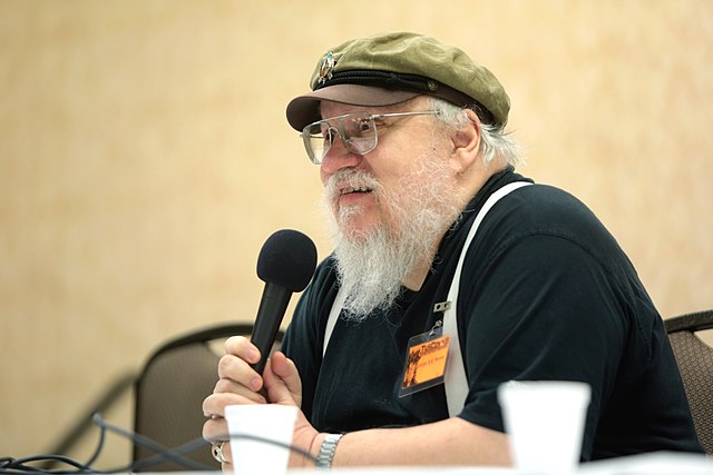 George R. R. Martin is sitting at a char with a microphone. He is among the authors who have filed the lawsuit and partnered with the Authors Guild. 