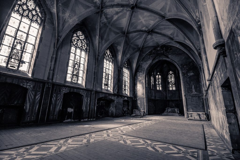 A decrepit-looking church with big windows, rugs, and an empty entryway.