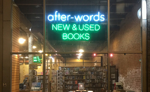 glass window looking in on shelves with a blue and green neon sign