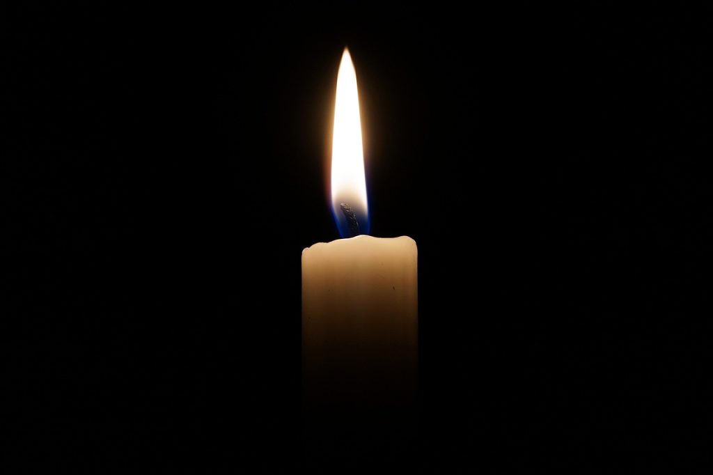 A dark background with a candle in focus, the wick lit with a big flame.