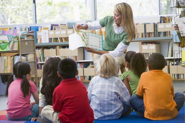Woman reading to a group of kids in a library.