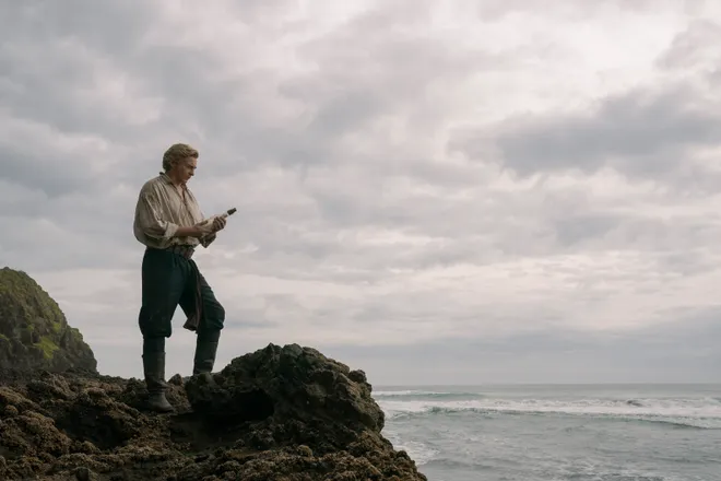 Rhys Darby as Stede Bonnet standing on a rocky shore in Our Flag Means Death Season 2
