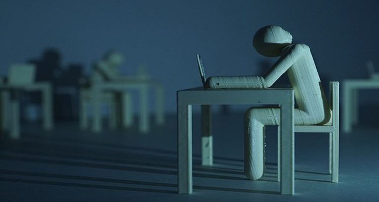 A block-person sitting on their computer, head down, symbolizing the struggle to cope with artificial intelligence in the workplace.
