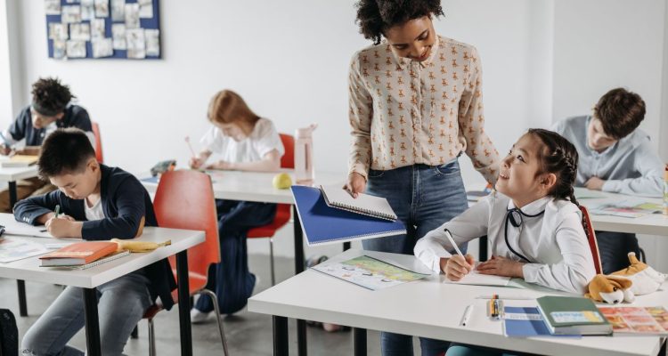 A teacher helping one student while four others work at their tables