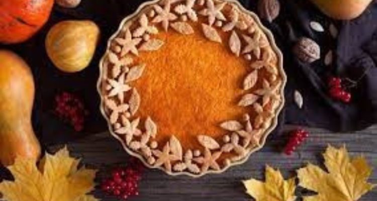 Closeup image of a pumpkin pie with gourds and leaves surrounding it