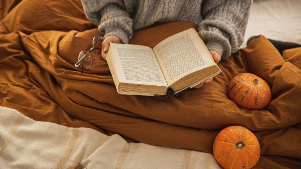 Comfortably reading a book in bed with pumpkins laying around
