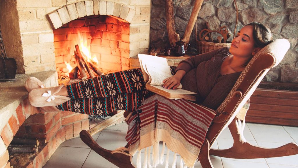 Woman reading next to a fireplace 
