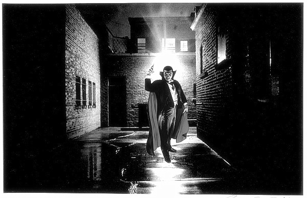 A vampire stands in a dark alley and threatens the camera with an outstretched arm
