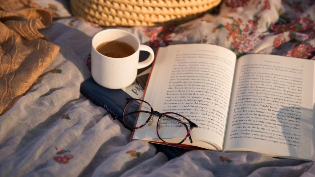book open on a blanket with glasses and a cup of tea