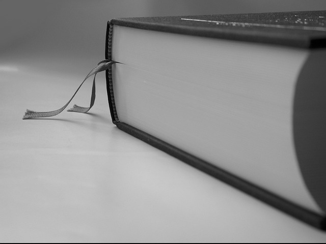 A black and white image of a closed book with a book ribbon sticking out between the pages.