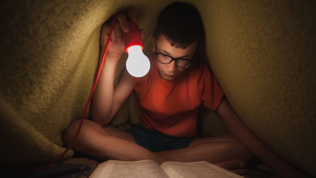 boy reading under blanket with light
