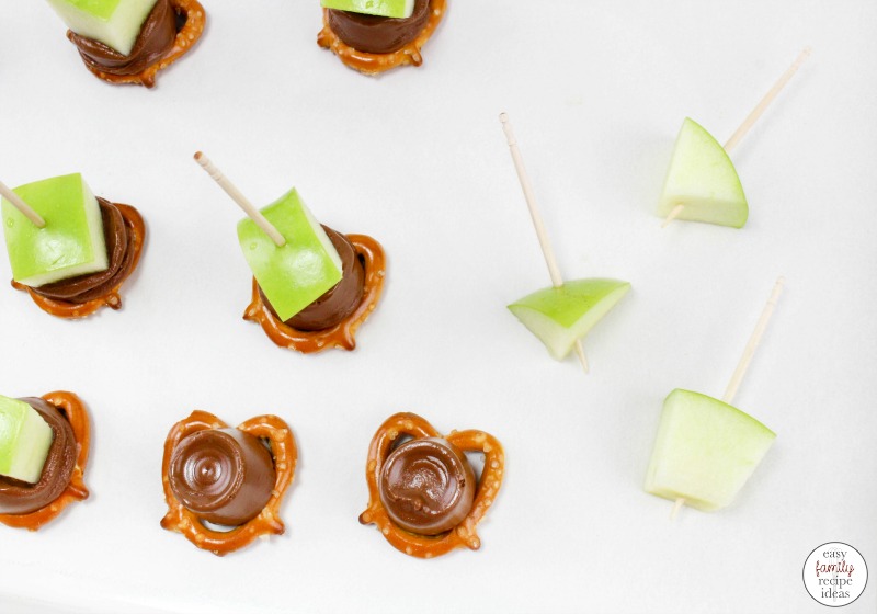A bunch of pretzels with caramel on top and green apple chunks in toothpicks