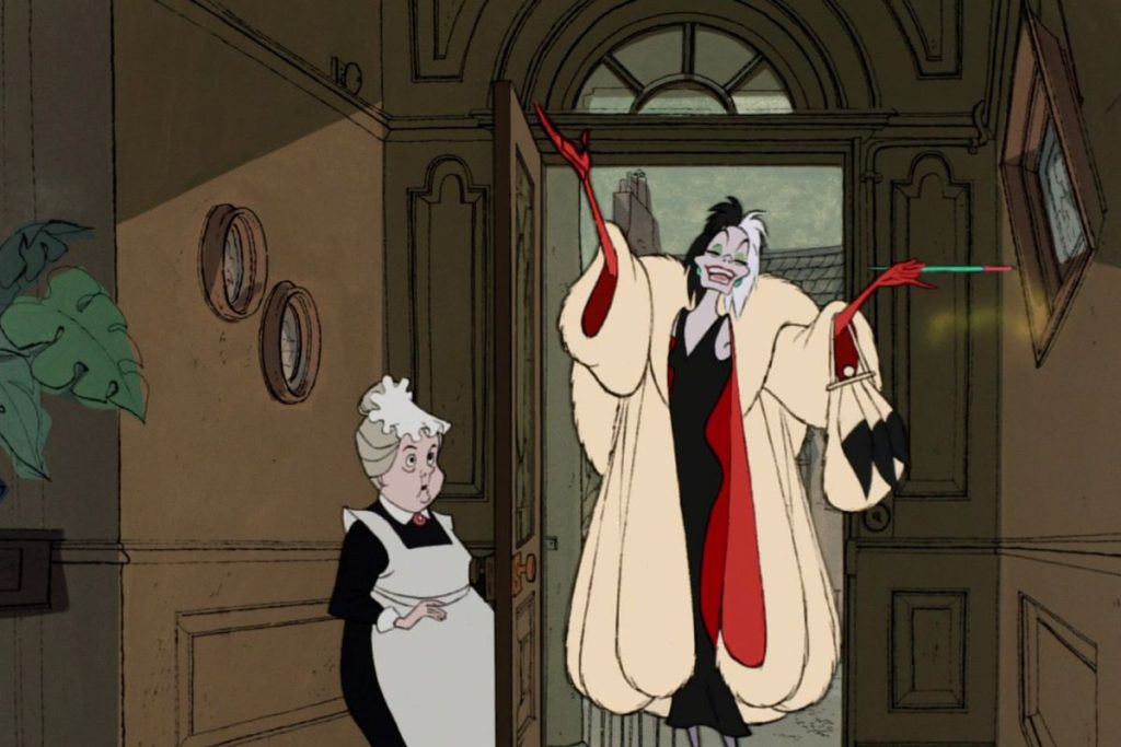Cruella De Vil in a cream and red coat with a black dress underneath next to a maid.