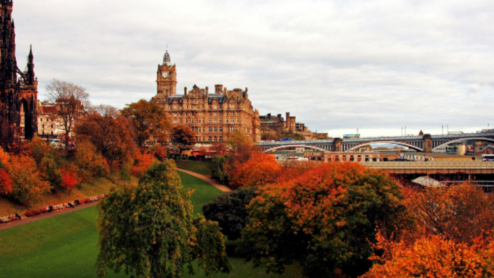 Fall foliage featuring a bridge and a large building of Scottish architecture