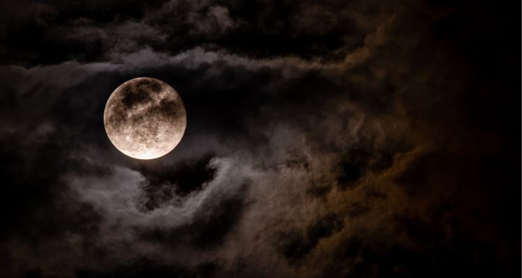 A moon shows through dark, storm-like clouds.
