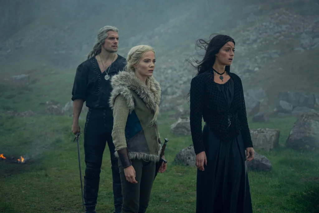 Geralt in a black shirt and pants, Ciri in a fur coat, and Yennefer in a black dress. All of them are looking off into the distance.