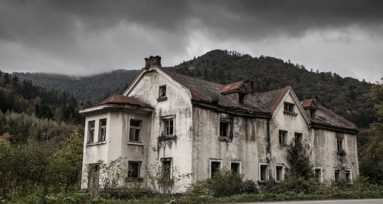 Vintage, seemingly abandoned mansion set in a gloomy area with dark skies above it. There's an ominous, creeping feeling.