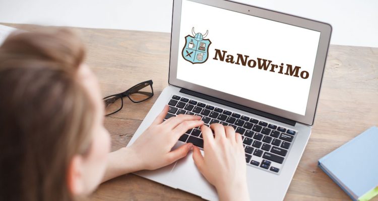 A woman typing on her laptop, which has the NaNoWriMo logo of a mint green shield on it.