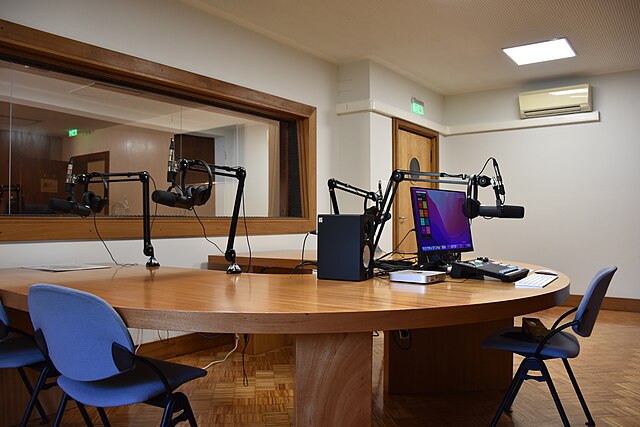 Large podcast studio with rounded table, four microphones, and a computer.