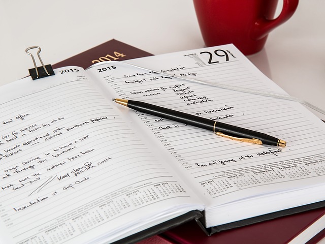 A calendar planner from 2015 open to a random page with a black and gold pen sitting on top. There is a red mug next to the book.