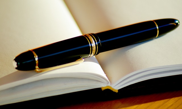 A black and gold pen sitting on top of a blank book.
