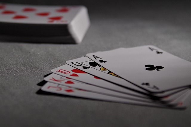 A set of playing cards on a gray surface. The cards near the camera are a Jack, a King, a ten, a Queen, and an Ace.